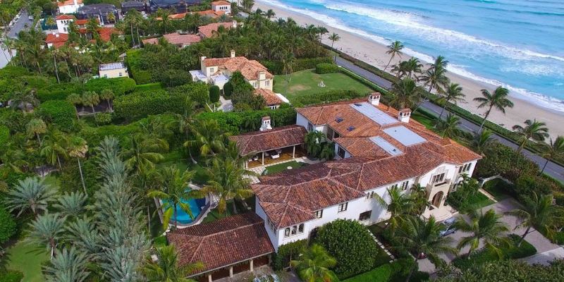 An aerial view of a luxury Mediterranean-style mansion with a terracotta roof situated along the sandy Palm Beach coastal area.