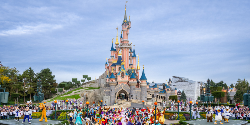 Disneyland Paris Castle with a crowd of visitors and Disney characters in colorful costumes, showcasing one of the top tourist attractions in France.