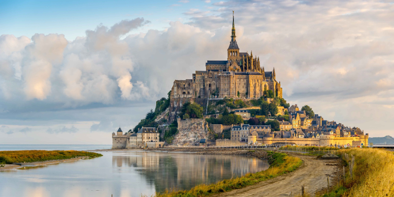 Aerial view of Mont Saint-Michel, a historic tourist attraction in France, surrounded by water and dramatic clouds.