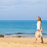 A woman in a white dress strolls along the beach, enjoying a sunny day in California.