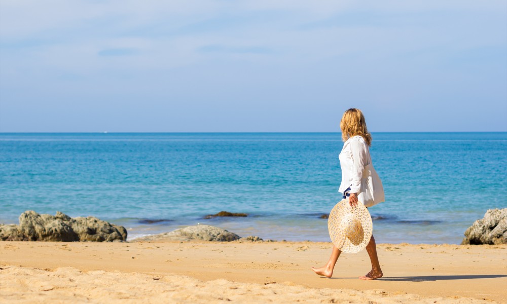 A woman in a white dress strolls along the beach, enjoying a sunny day in California.