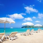 White loungers and umbrellas on a pristine beach with turquoise waters and clear blue skies represent the relaxing atmosphere of vacation islands in Florida.