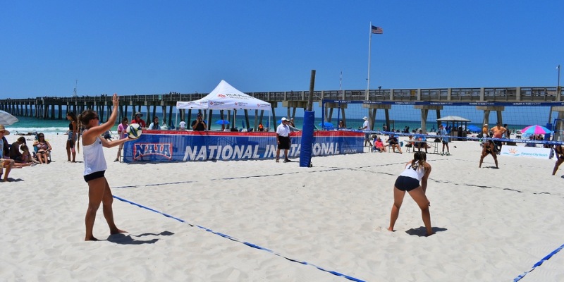 A vibrant scene from a beach volleyball game, showcasing tourists competing on a sandy court under a clear sky.