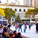 A group of people skating on an ice rink, with a large building visible in the background.