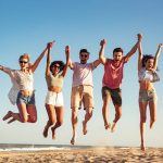 A group of friends joyfully jumping together on a sandy beach, capturing a moment of happiness and camaraderie.