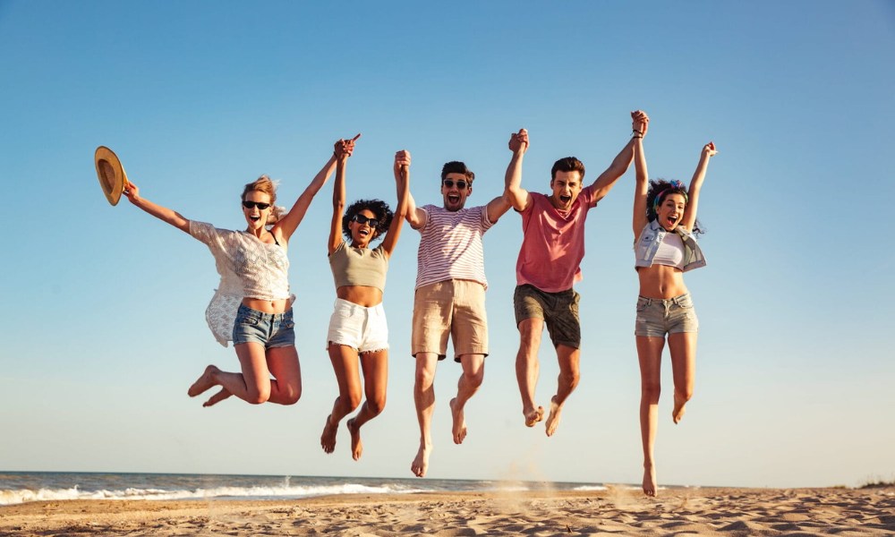 A group of friends joyfully jumping together on a sandy beach, capturing a moment of happiness and camaraderie.