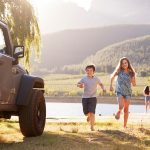 A cheerful family dashes to a jeep near a tranquil lake, embodying the excitement of exploring California in December.