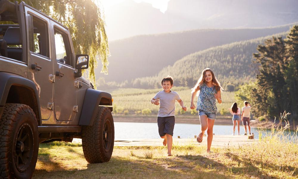 A cheerful family dashes to a jeep near a tranquil lake, embodying the excitement of exploring California in December.