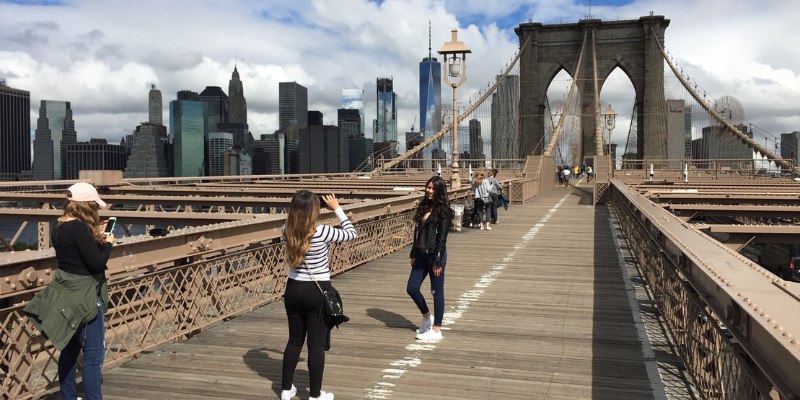 Three friends taking pictures on the Brooklyn Bridge, framed by the impressive architecture and vibrant city scenery.