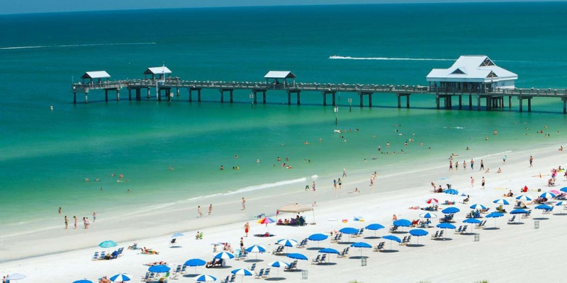 A lively beach populated with sunbathers and swimmers, complemented by a pier that juts out into the sea.