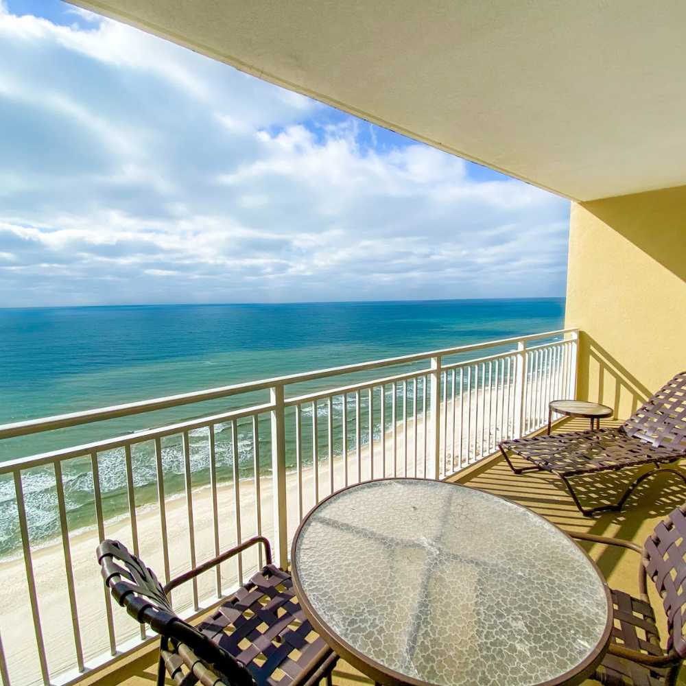 Two chairs and a table on a balcony, provide a picturesque view of the beach.