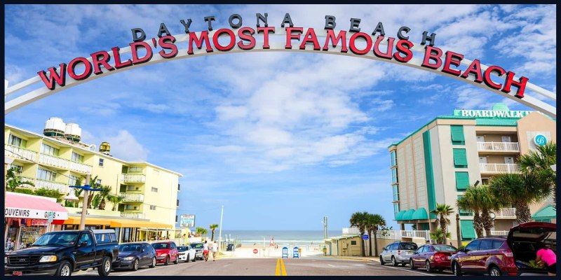 The entrance arch at Daytona Beach, labeled "World's Most Famous Beach," with surrounding buildings and parked cars.