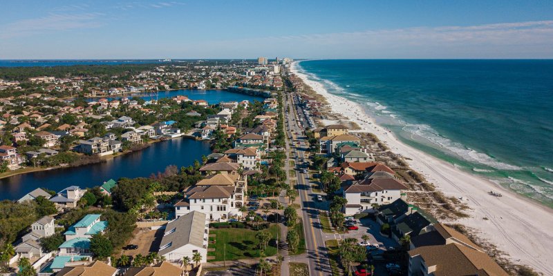 Aerial view showcasing a picturesque Destin Harbor Boardwalk with houses lining the shore, highlighting the coastal landscape.