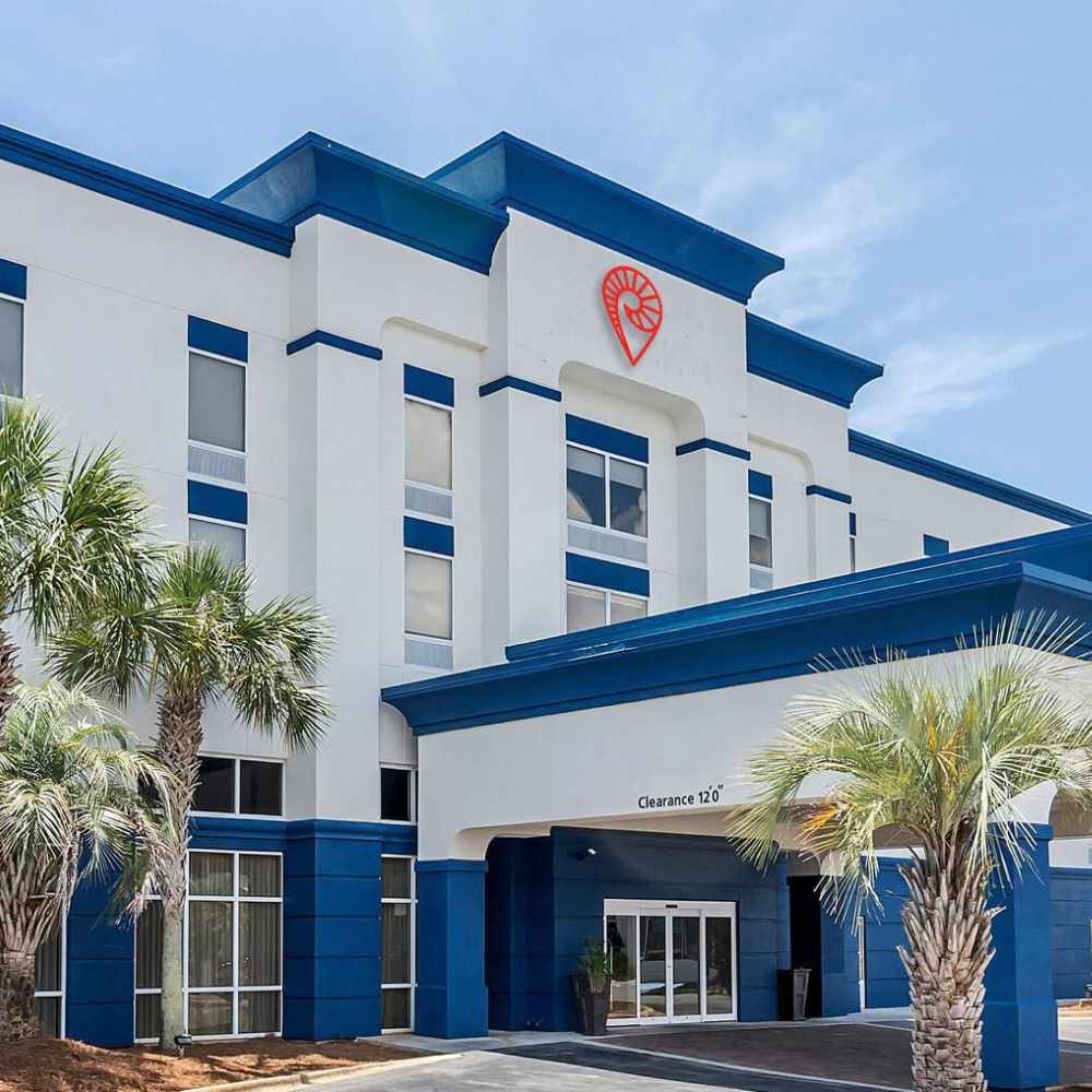 Exterior view of a hotel in Destin Florida, featuring palm trees and a blue and white facade, perfect for a getaway.