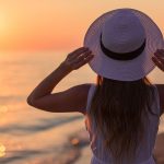 A woman in a stylish hat looks up at the sun, basking in its radiant glow and warmth