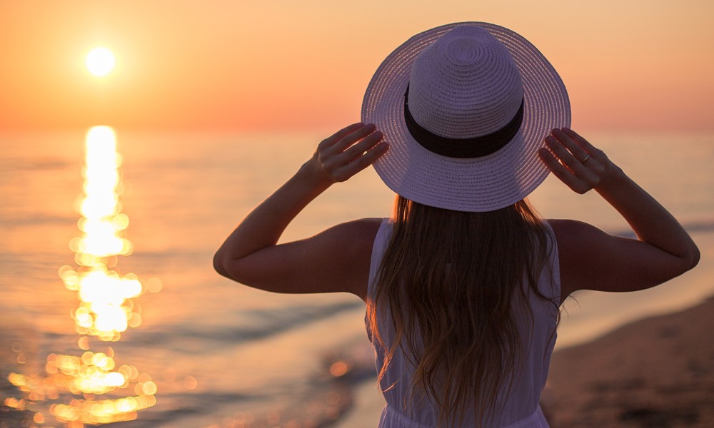 A woman in a stylish hat looks up at the sun, basking in its radiant glow and warmth