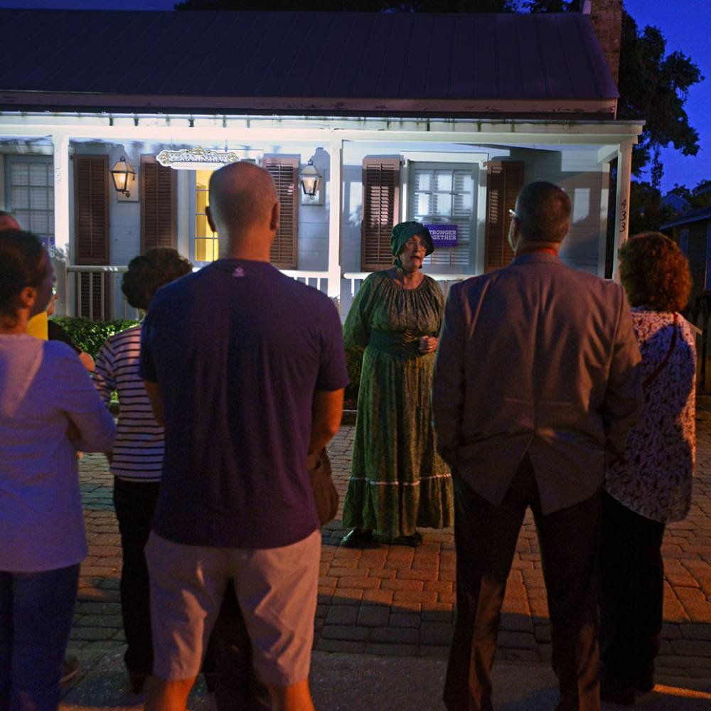 A lively group enjoys a night outside a house, reminiscing about their spooky bus tour and ghost stories in Pensacola.