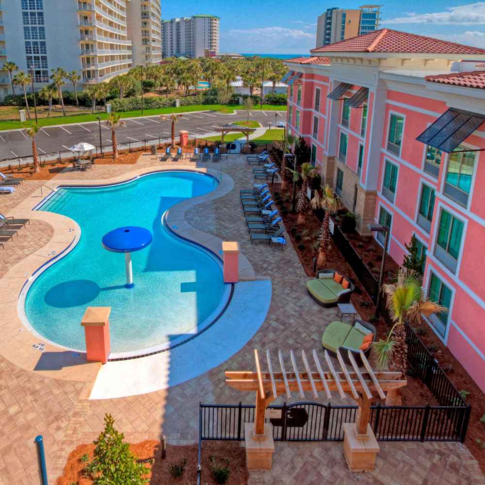 Aerial view of a hotel pool with surrounding deck chairs in Destin, Florida, showcasing a vibrant area for relaxation and leisure.