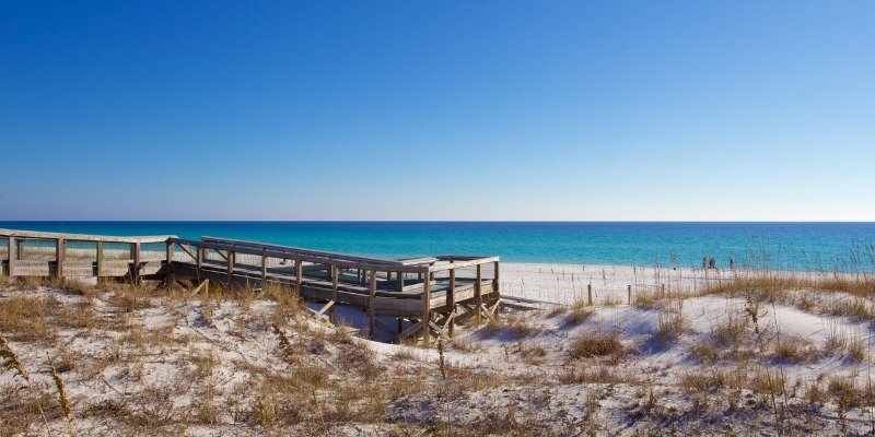 A picturesque beach with a wooden pathway guiding visitors to the calm waters of the ocean.