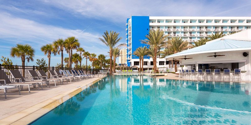 A serene beachfront resort pool in Clearwater, Florida, surrounded by palm trees and clear blue skies.