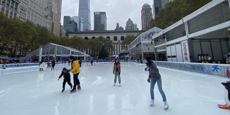 People glide across an ice rink, set against a backdrop of buildings, showcasing a vibrant winter activity.