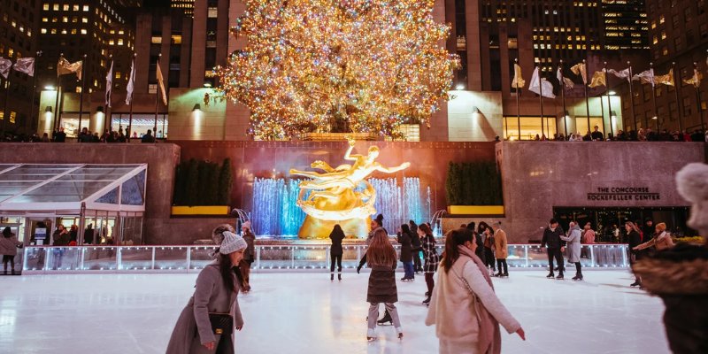 A festive scene of people skating on ice, with a beautifully decorated Christmas tree in the background.