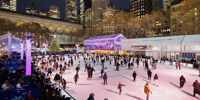 Skaters enjoy a lively day on the ice rink in Bryant Park, set against the backdrop of the bustling city.