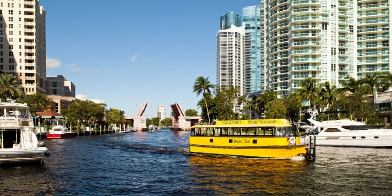 A yellow boat moves along a canal, surrounded by impressive tall buildings lining the waterway.