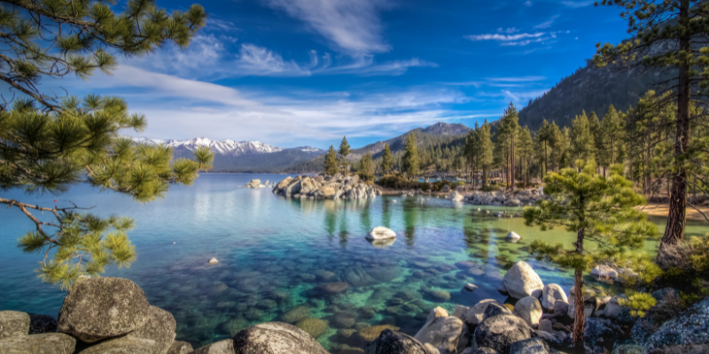 Majestic mountains surround clear blue Lake Tahoe under a bright sky.