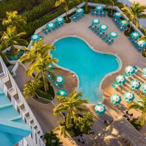 View of a beautiful pool at a beach club resort, framed by lush greenery and sandy shores.