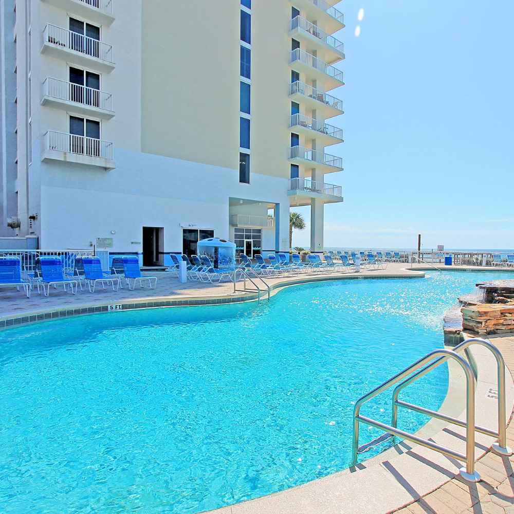 A serene beachfront pool at a condo, surrounded by palm trees and clear blue skies.