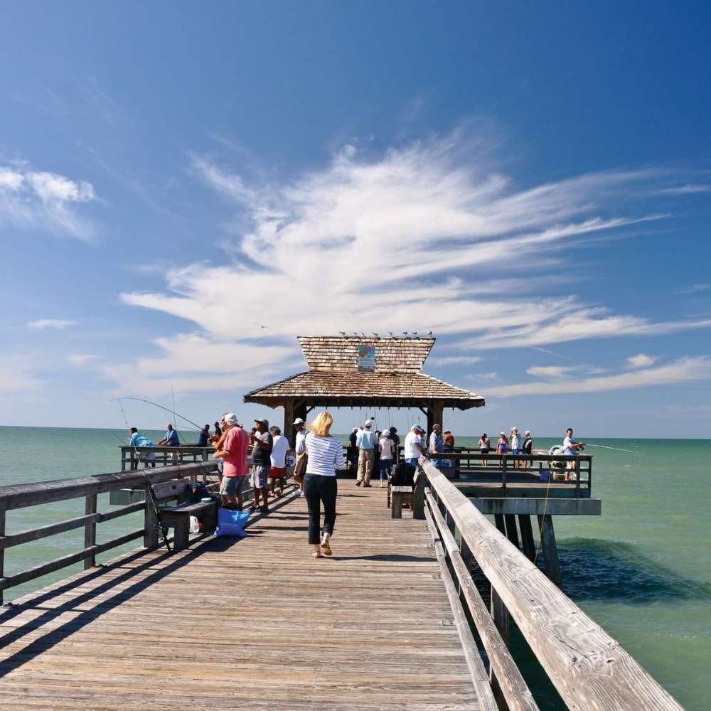 People enjoy a leisurely walk on the Naples Pier, immersed in the scenic beauty and vibrant energy of the location