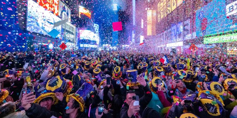 People cheer and celebrate New Year's Eve in Times Square, surrounded by colorful lights and a festive atmosphere.