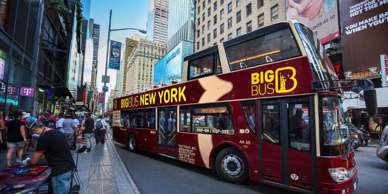 A double-decker bus featuring a prominent New York sign, promoting the New York Hop On Hop Off Tours.