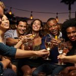 A group of friends enjoying a night out in Destin, Florida, clinking glasses and smiling under string lights.