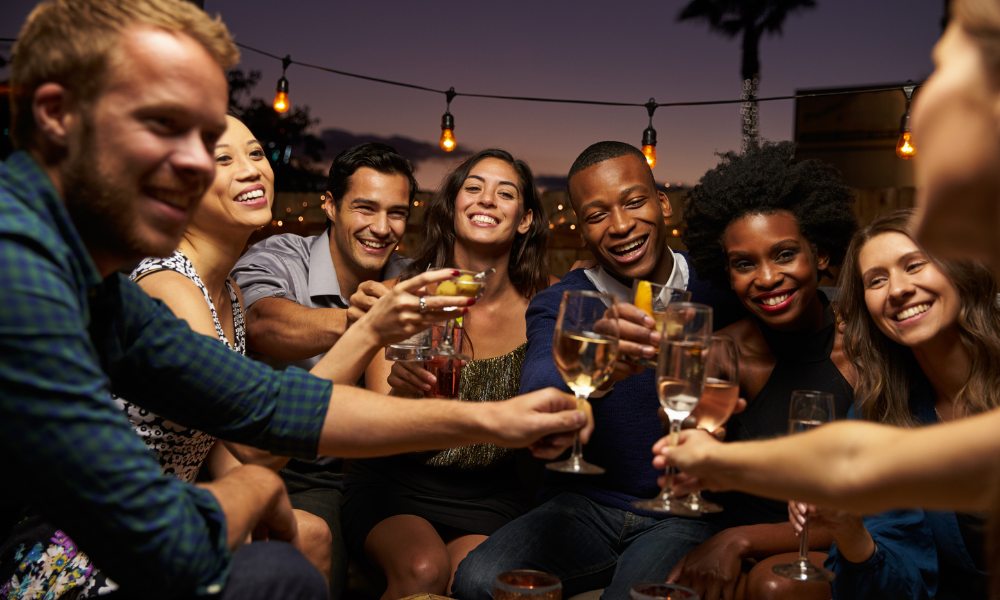 A group of friends enjoying a night out in Destin, Florida, clinking glasses and smiling under string lights.