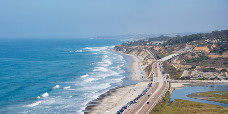 Overhead shot of the Pacific Coast Highway winding along the ocean, with a beautiful beach in view.