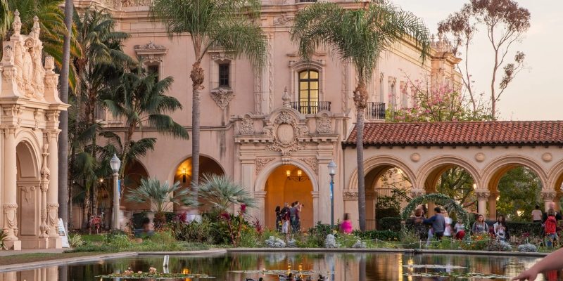 In Balboa Park, a woman enjoys the view of a fountain in a charming courtyard, with vibrant gardens and museums nearby.