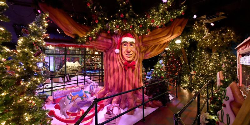 A festive tree adorned with lights is accompanied by a man in a suit, celebrating the magic of Santa at Santaland.