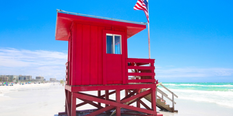 Red lifeguard tower with an American flag on Siesta Key Beach, Florida, with turquoise waters and a clear blue sky in the background.