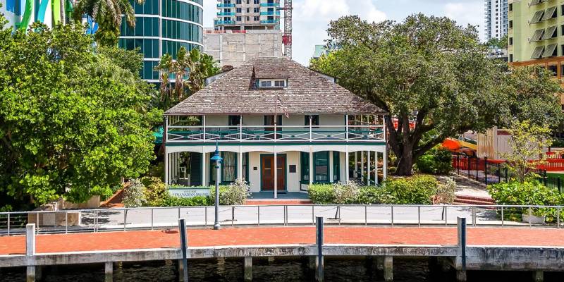 A serene house on the water, framed by towering buildings in the background, showcasing urban and natural harmony.