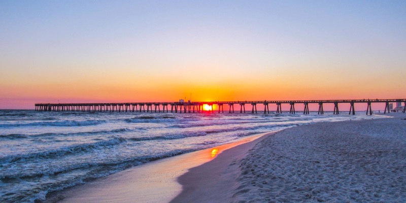 A picturesque sunset casts warm hues over the Panama beach and pier, creating a serene coastal scene.