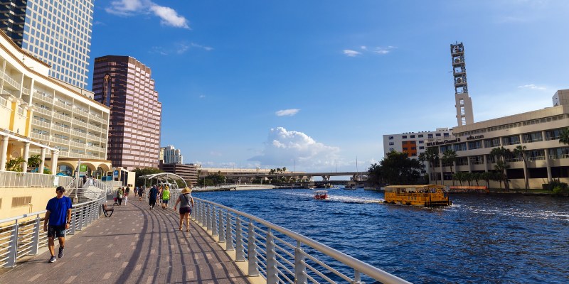 People stroll along a scenic boardwalk beside a tranquil river, enjoying the natural surroundings and fresh air.