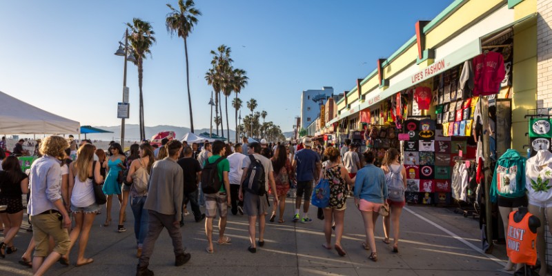 People walk along the Venice Beach Boardwalk, surrounded by lively activity and the scenic beauty of the beach.