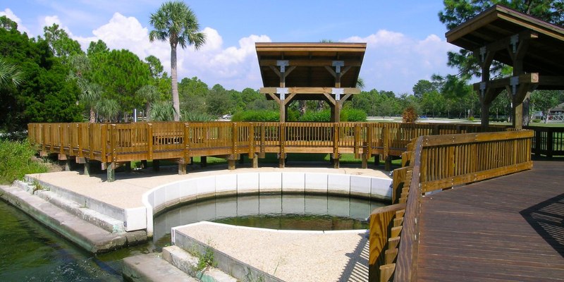 A picturesque wooden deck beside a calm pond, featuring a rustic wooden bridge for crossing.