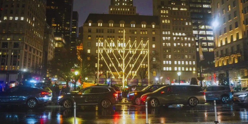 Nighttime city street scene with cars and buildings, showcasing the festive atmosphere of the World’s Largest Menorah Lighting.