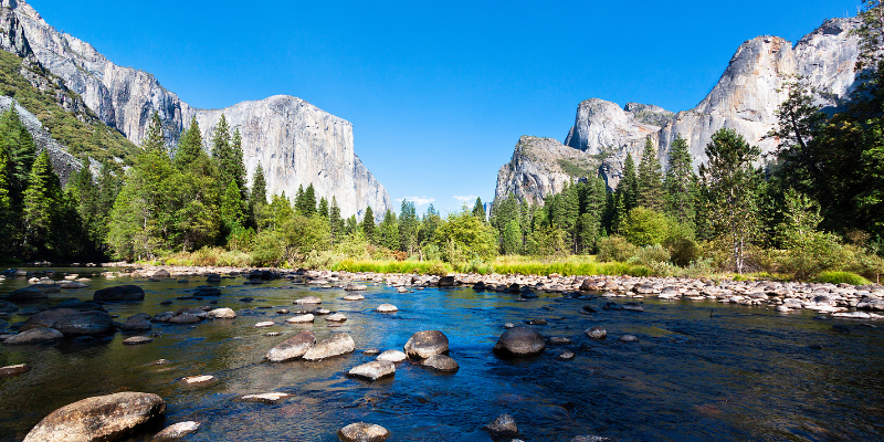 A river flows through a rocky landscape, framed by majestic mountains in Yosemite National Park.