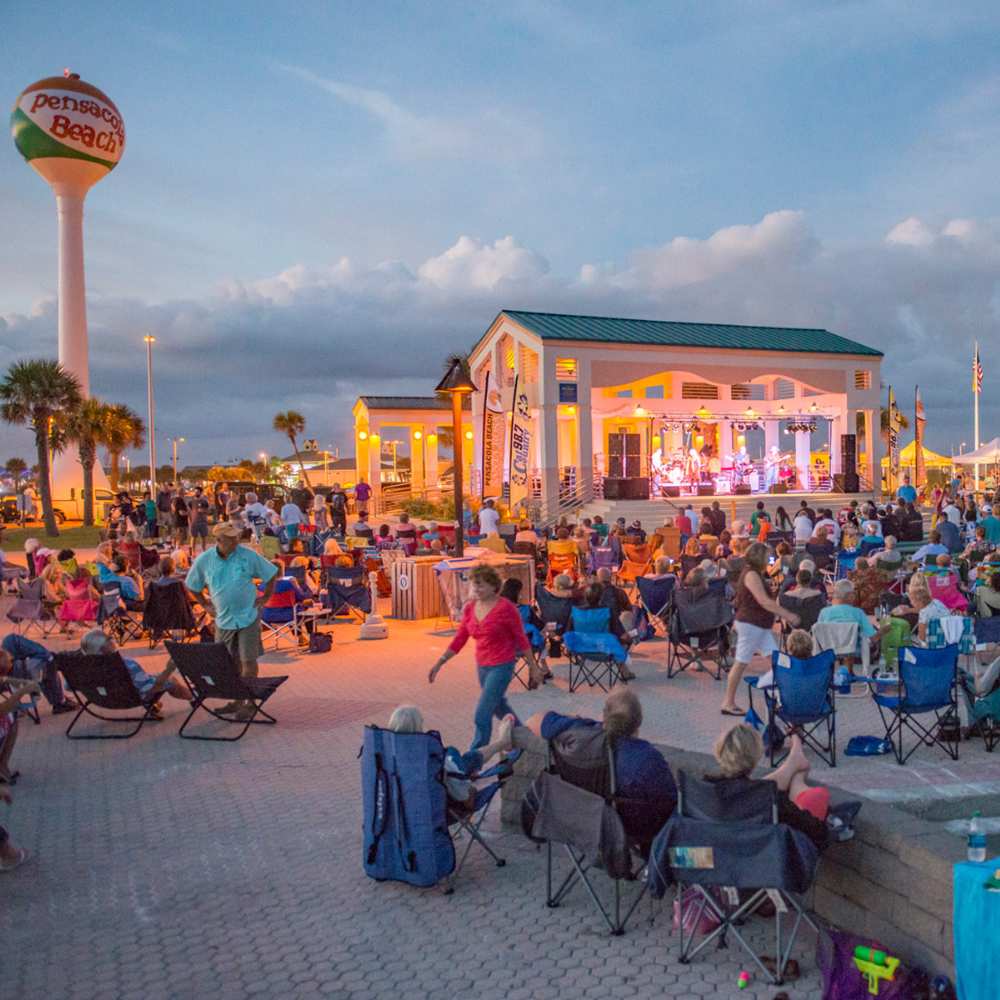 A gathering of individuals in lawn chairs watches the sunset, surrounded by the beauty of Pensacola's sandy beaches.