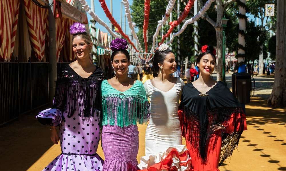 Three women in traditional Spanish dresses pose together for a photograph, showcasing vibrant colors and intricate designs.