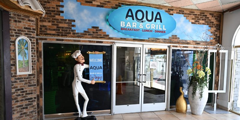 Entrance to Aqua Bar & Grill featuring a welcoming sign and outdoor seating area with vibrant decor.